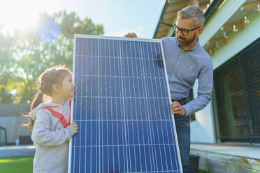 Vater mit seiner kleinen Tochter in der Nähe des Hauses mit Sonnenkollektoren. Alternative Energie, Ressourcenschonung und nachhaltiger Lebensstil. - HPIF11752