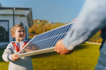 Ein Vater mit seiner kleinen Tochter fängt die Sonne an einem Solarmodul ein und lädt es im Garten auf. Alternative Energie, Ressourcenschonung und nachhaltiger Lebensstil. - HPIF11760