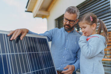 Ein Vater zeigt seiner kleinen Tochter die Funktionsweise von Photovoltaikmodulen und erklärt ihr, wie alternative Energie, Ressourcenschonung und nachhaltiger Lebensstil funktionieren. - HPIF11762