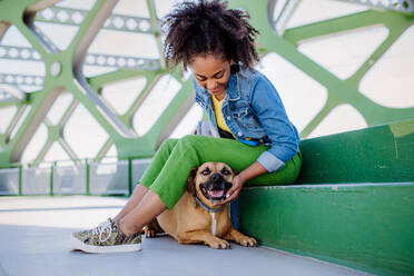 Multirassisches Mädchen sitzt und ruht sich mit ihrem Hund draußen auf der Brücke aus, trainiert ihn, verbringt die Freizeit zusammen. Konzept der Beziehung zwischen einem Hund und Teenager, Alltag mit Haustier. - HPIF11860