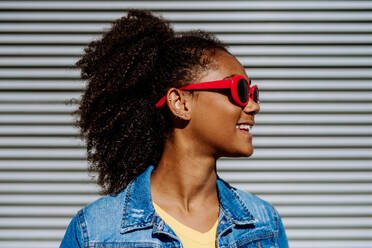 Portrait of young happy multiracial teenage girl with red sunglasses and afro hairstyle, standing outdoor. - HPIF11879