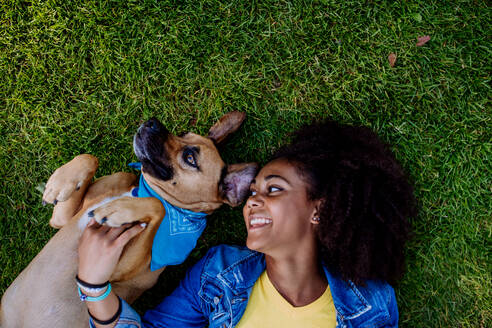 Draufsicht auf ein multirassisches Teenager-Mädchen und ihren Hund, die auf einer Wiese im Stadtpark liegen, Konzept der Beziehung zwischen Hund und Teenager, alltägliches Leben mit Haustier. - HPIF11884
