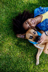 Top view of happy multiracial teenage girl with her dog lying in the grass. Concept of relationship between dog and teenager, everyday life with a pet, canis therapy. - HPIF11885