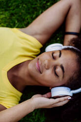 Multiracial girl lying down in a grass and enjoying music in headphones, top view. - HPIF11891