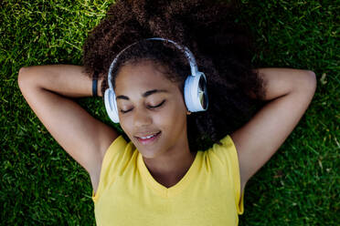Multirassisches Mädchen liegt im Gras und genießt Musik aus Kopfhörern, Ansicht von oben. - HPIF11892