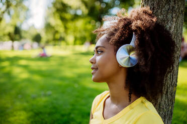 Multiracial girl sitting in a grass and enjoying music in headphones, side view. - HPIF11893