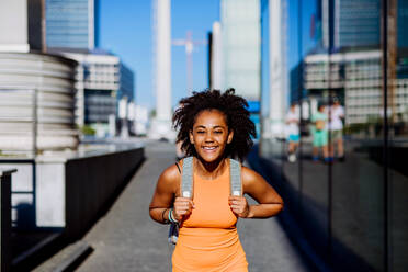 Multiracial teenage girl walking with a backpack in modern city centre during summer day, back to school concept. - HPIF11899