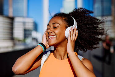 Multirassisches Mädchen, das bei einem Stadtspaziergang Musik mit Kopfhörern hört. - HPIF11901