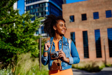 Multirassisches Mädchen, das mit einer Kamera durch eine Stadt läuft und Fotos macht. - HPIF11908