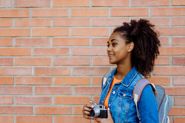Multirassisches Teenager-Mädchen mit Rucksack und Skateboard, vor einer Backsteinmauer. - HPIF11913