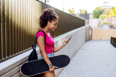 Multiracial Teenager-Mädchen mit Rucksack und Skateboard, zu Fuß in der Stadt während eines Sommertages. - HPIF11917