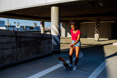 Multiracial teenage girl skateboarding in modern city during summer day. - HPIF11925