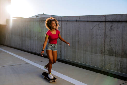 Multirassisches Teenager-Mädchen fährt Skateboard vor einer Betonmauer, balancierend, Seitenansicht. - HPIF11926