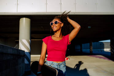 Multiracial Teenager-Mädchen zu Fuß mit einem Skateboard in der modernen Stadt im Sommer Tag. - HPIF11927