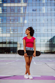 Multiracial Teenager-Mädchen mit Rucksack und Skateboard, zu Fuß in der Stadt während eines Sommertages. - HPIF11928