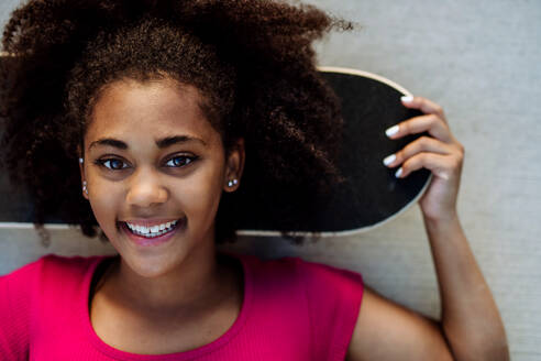 Multirassisches Teenager-Mädchen mit Skateboard vor einer Betonwand an einem Sommertag. - HPIF11929