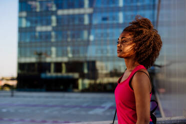 Multirassisches Teenager-Mädchen, das während des Sonnenuntergangs im modernen Stadtzentrum spazieren geht, Seitenansicht. - HPIF11937