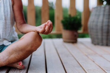 Nahaufnahme einer Meditationshaltung einer Frau, die auf einer Terrasse sitzt. - HPIF11987