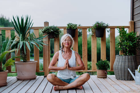 Senior woman sitting outdoors on a terrace in summer, doing yoga exercise. - HPIF11988