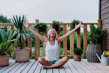 Senior woman sitting outdoors on a terrace in summer, doing yoga exercise. - HPIF11991