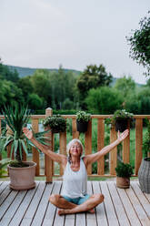Ältere Frau, die im Sommer auf einer Terrasse sitzt und Yogaübungen macht. - HPIF11992