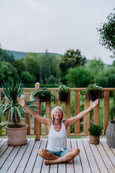 Senior woman sitting outdoors on a terrace in summer, doing yoga exercise. - HPIF11992