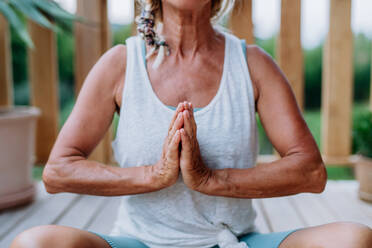 Ältere Frau, die im Sommer auf einer Terrasse sitzt und Yogaübungen macht. - HPIF12006