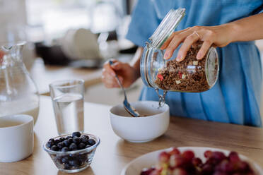 Nahaufnahme einer jungen Frau, die in ihrer Küche ein Müsli zum Frühstück zubereitet, Morgenroutine und gesunder Lebensstil. - HPIF12011