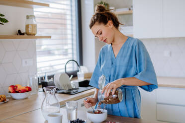 Junge Frau, die in ihrer Küche ein Müsli zum Frühstück zubereitet, morgendliche Routine und gesundes Lebenskonzept. - HPIF12012