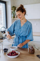 Junge Frau, die in ihrer Küche ein Müsli zum Frühstück zubereitet, morgendliche Routine und gesundes Lebenskonzept. - HPIF12015