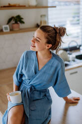 Junge Frau genießt eine Tasse Kaffee am Morgen in einer Küche. - HPIF12021