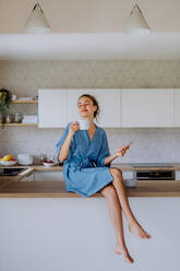 Junge Frau genießt eine Tasse Kaffee am Morgen in einer Küche. - HPIF12023