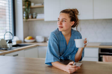 Young woman with smartphone enjoying cup of coffee at morning, in a kitchen. - HPIF12024