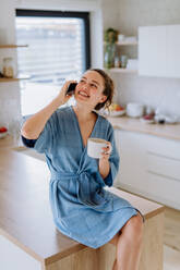 Junge Frau ruft an und genießt eine Tasse Kaffee am Morgen, in einer Küche. - HPIF12027