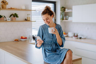 Young woman with smartphone enjoying cup of coffee at morning, in a kitchen. - HPIF12028