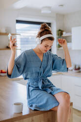 Junge Frau genießt eine Tasse Kaffee und hört Musik am Morgen in einer Küche. - HPIF12031