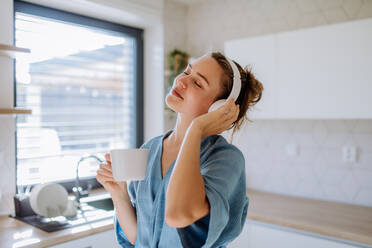 Young woman enjoying cup of coffee and listening music at morning, in a kitchen. - HPIF12034
