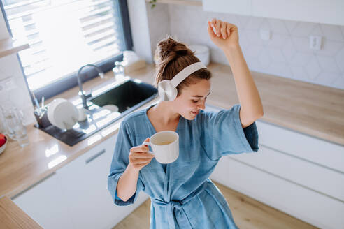 Junge Frau genießt eine Tasse Kaffee und hört Musik am Morgen in einer Küche. - HPIF12035