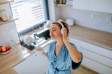 Junge Frau genießt eine Tasse Kaffee und hört Musik am Morgen in einer Küche. - HPIF12037