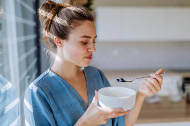 Young woman having a muesli for breakfast in her kitchen, morning routine and healthy lifestyle concept. - HPIF12040