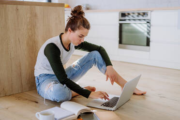 Junge Frau sitzt mit Laptop und einer Tasse Kaffee in ihrer Küche. - HPIF12042