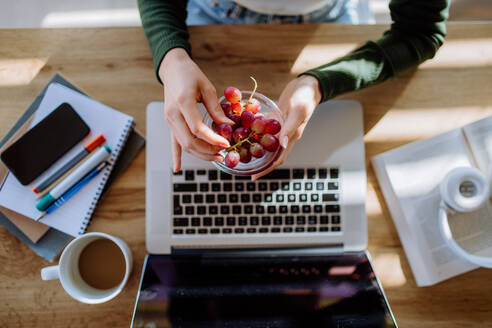 Draufsicht auf eine Frau, die eine Schale mit Weintrauben über einem Schreibtisch mit Computer, Tagebuch und Smartphone hält. Work-Life-Balance-Konzept. - HPIF12072