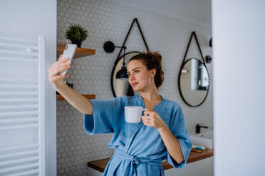 Young woman taking selfie in bathroom, enjoying a cup of coffee. - HPIF12135