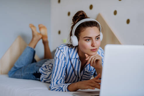 Junge Frau ruht sich auf einem Bett aus und lauscht der Musik. - HPIF12145