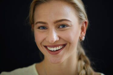 Porträt einer schönen blonden jungen Frau, die in die Kamera schaut und auf schwarzem Hintergrund lächelt, Nahaufnahme - HPIF12179