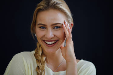 Porträt einer schönen blonden jungen Frau, die in die Kamera schaut und auf schwarzem Hintergrund lächelt, Nahaufnahme - HPIF12181