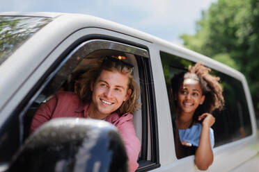 Junge, gemischtrassige Freunde, die zusammen im Auto unterwegs sind, durch das Fenster schauen und lächeln - Sommerurlaub, Ferien, Reisen, Roadtrip und Menschen Konzept. - HPIF12189