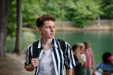 Ein Porträt eines jungen Mannes mit Freunden im Hintergrund auf einer Wanderung oder einem Campingausflug in den Bergen im Sommer. - HPIF12206