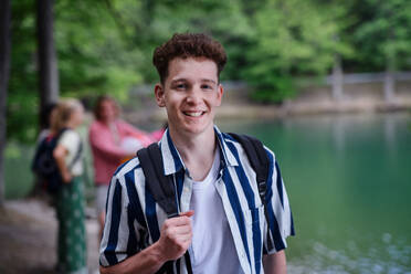 Ein Porträt eines jungen Mannes mit Freunden im Hintergrund auf einer Wanderung oder einem Campingausflug in den Bergen im Sommer. - HPIF12207