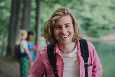 Ein Porträt eines jungen Mannes mit Freunden im Hintergrund auf einer Wanderung oder einem Campingausflug in den Bergen im Sommer. - HPIF12213